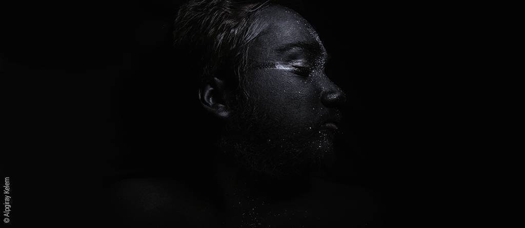 Foto: Ein im schwarzen Hintergrund versinkendes sehr dunkles und mystisch wirkendes kindliches Gesicht.